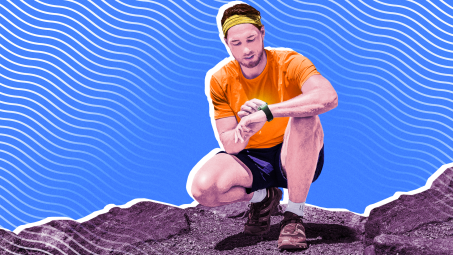 A man kneeling on a rocky surface and checking his fitness tracker
